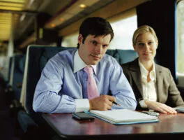 Businessman and businesswoman on train, smiling, portrait